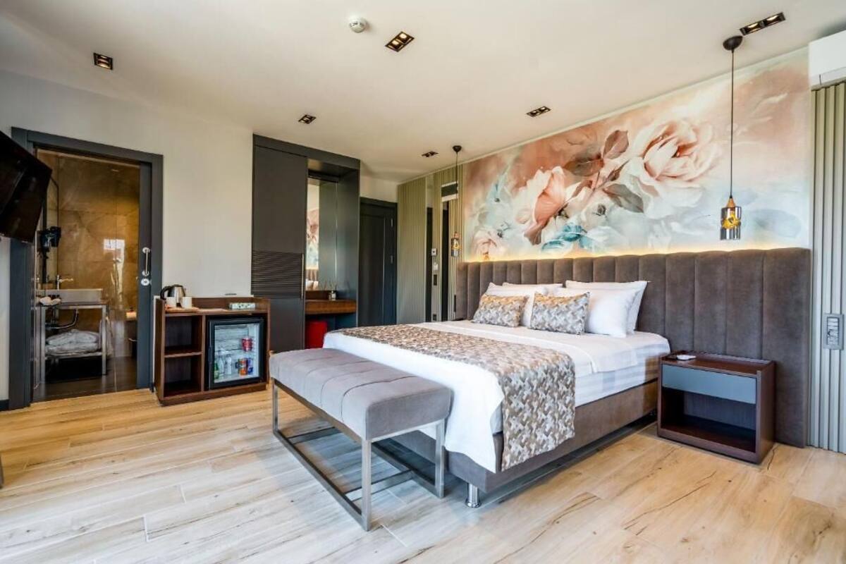 A modern bedroom with a large bed, a bench, a small bedside table, a wall-mounted TV, and a floral mural.