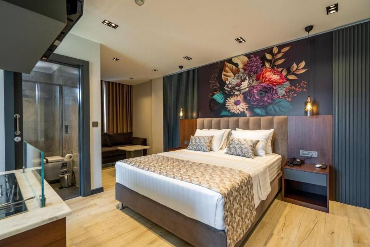 A modern hotel room with a large bed, a desk with a chair, a bathroom, and a decorative wall mural.