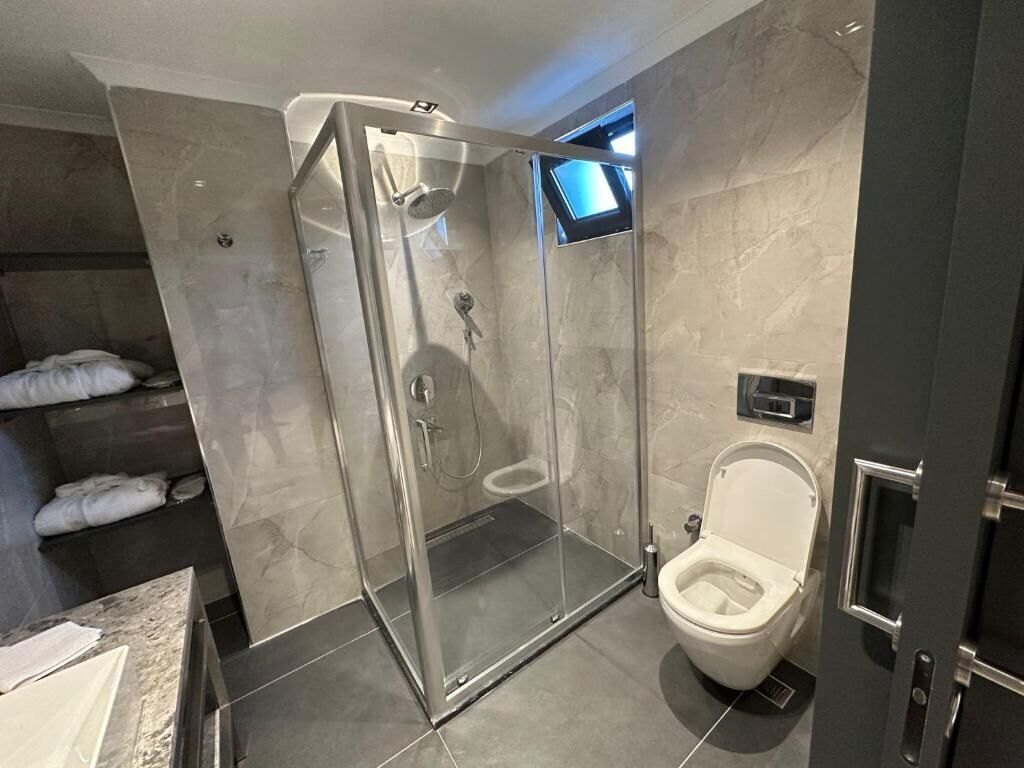 Un baño moderno con ducha envuelta en vidrio, un inodoro y una ventana pequeña.