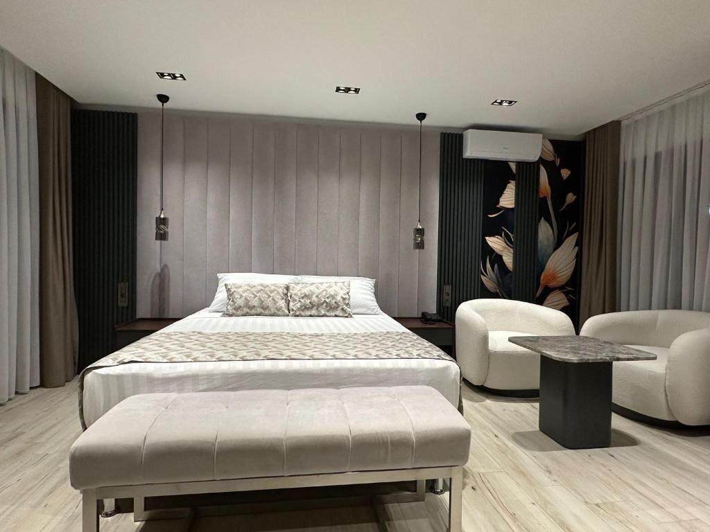 Un dormitorio moderno con cama, banca, sillón y una mesita.