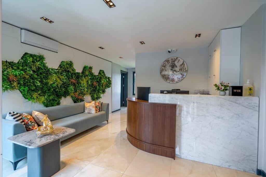 A modern reception area with a marble counter, a grey sofa, a wall-mounted clock, and a green wall feature.