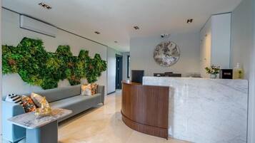 Un espace d’accueil moderne avec un comptoir en marbre, un canapé gris, une horloge murale et un mur décoratif vert.