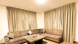 A living room with a sectional sofa, a coffee table, and curtains. - Central Apartment For Rent 30 (Amman)