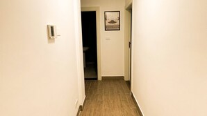 A hallway with a wooden floor, white walls, a ceiling light, and a framed picture on the wall. - Central Apartment For Rent 30 (Amman)