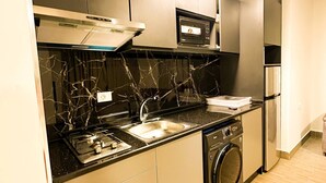 A compact kitchen with a stove, sink, microwave, and a built-in washing machine. - Central Apartment For Rent 30 (Amman)