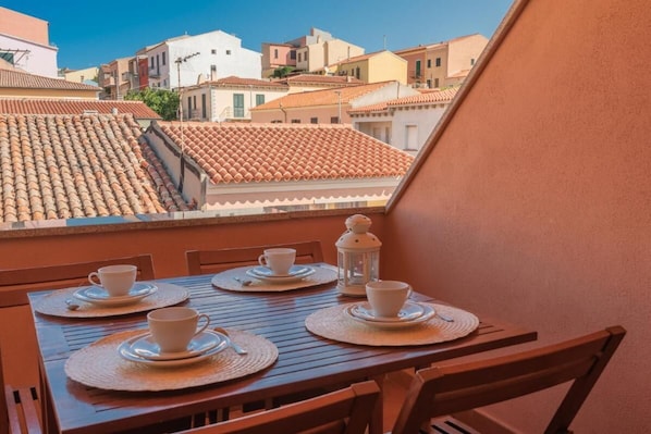 Un balcon avec une table dressée pour deux personnes, offrant une vue sur le paysage urbain et ses toits de tuiles.