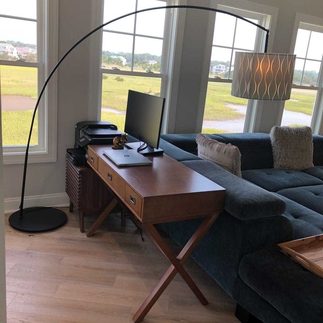 Un salon moderne avec un bureau en bois, un canapé foncé et une grande fenêtre donnant sur l’extérieur.