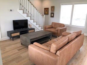 A living room with a sofa, a coffee table, a TV, and a staircase. - Sun-kissed Mermaid / 846 Ocean Blvd West 2 Bedroom Home by RedAwning (Supply)
