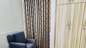 A hotel room with a bed, a chair, a wardrobe, and a curtain.