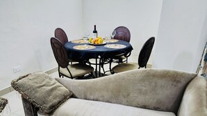A living room with a beige sofa, a dining table with chairs, and a small rug.