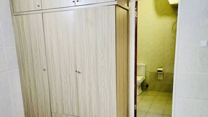 A room with a large wardrobe, tiled floor, and a doorway leading to a bathroom with yellow tiles.