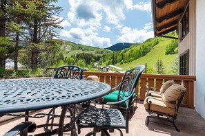 A patio with a round table and chairs, a wooden deck, and a view of green hills and a mountain. - Two-level corner condo w/ fireplace, amazing mountain views, spa and hot tub access (Vail)