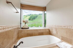 A bathroom with a bathtub, a window with a view of a green landscape, and a towel on the floor. - Two-level corner condo w/ fireplace, amazing mountain views, spa and hot tub access (Vail)