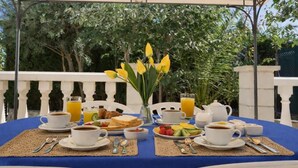 Een ontbijt opstelling op een blauwe tafel met witte stoelen, met croissants, fruit, koffie en sinaasappelsap.
