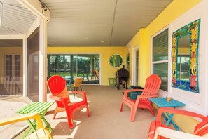 Uma área de varanda coberta com cadeiras e mesas coloridas, uma churrasqueira e vista para o exterior.