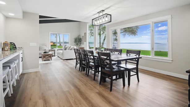Une cuisine spacieuse avec un coin repas, de grandes fenêtres offrant une vue sur la mer et un lustre moderne.