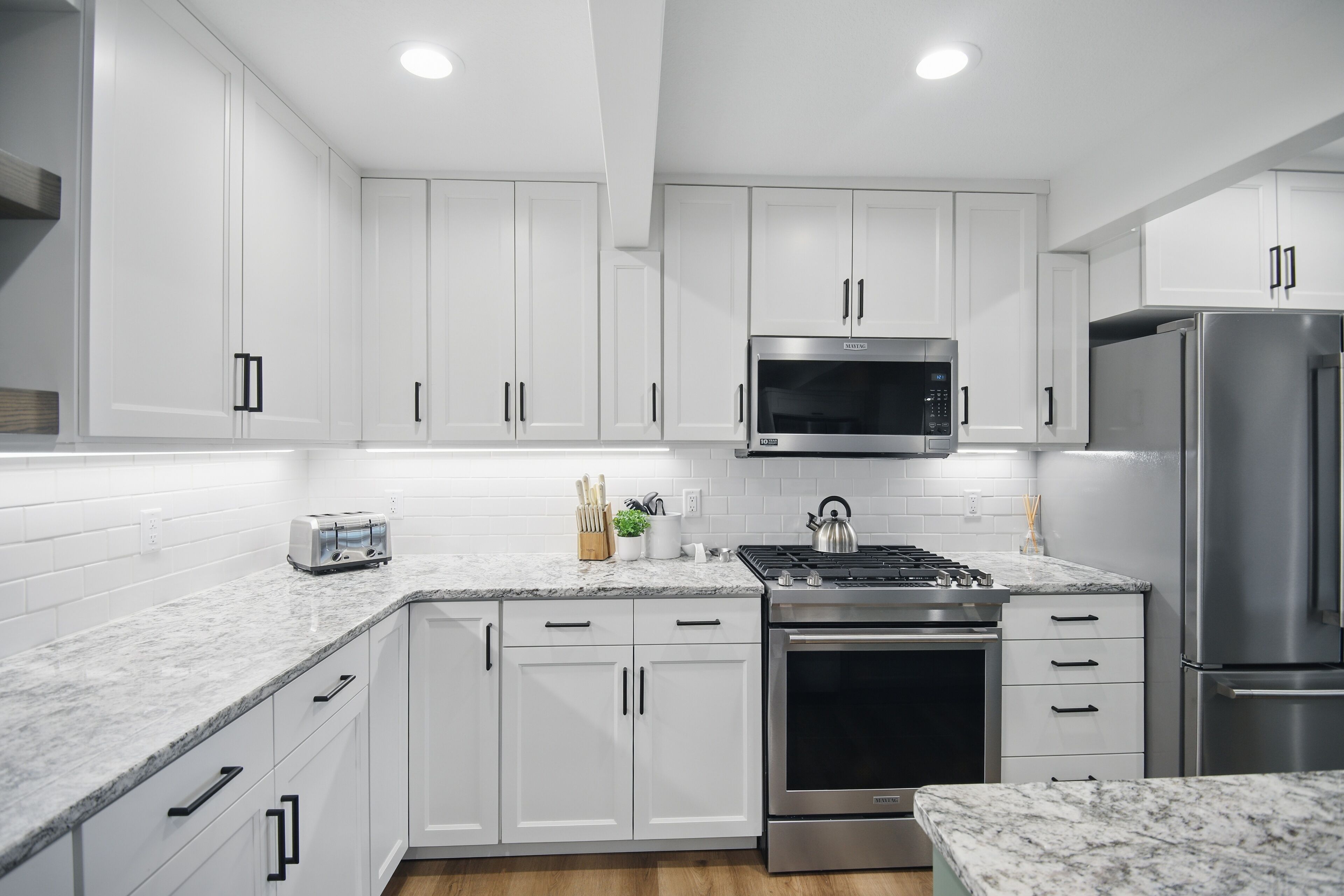 A modern kitchen with white cabinets, stainless steel appliances, a marble countertop, and a built-in oven.