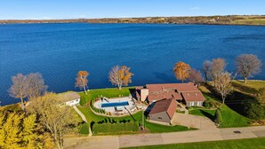 A residential property with a swimming pool, a large house, and a view of a lake. - Lakeside Getaway - Games, HotTub & Space to Gather (Faribault)