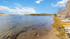 A clear lake with a wooden dock extending into the water, surrounded by trees and a distant shoreline.