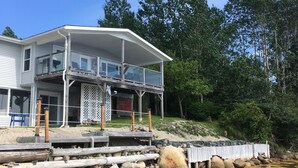 A waterfront house with a covered deck, a stone foundation, and a view of the water.