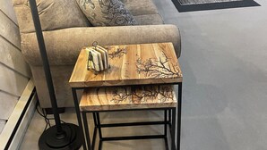 Ein gemütlicher Wohnbereich mit einer Couch, gemusterten Kissen, einem Couchtisch mit Holzmaserung und einer modernen Lampe.