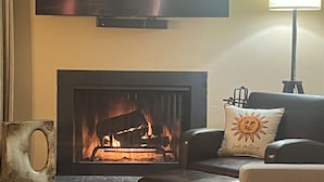 Ein Wohnzimmer mit Kamin, einem flachbildfernseher darüber, einem Sofa und einer Lampe.