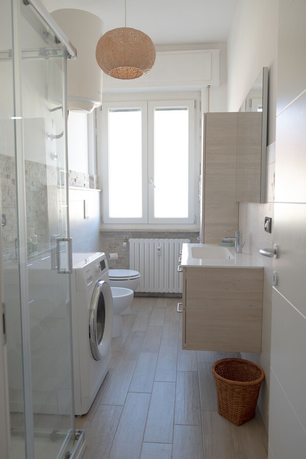 Une salle de bain moderne dotée d ’une douche à parois de verre, d’un lave-linge, de toilettes et d’un lavabo avec un meuble-vasque en bois.