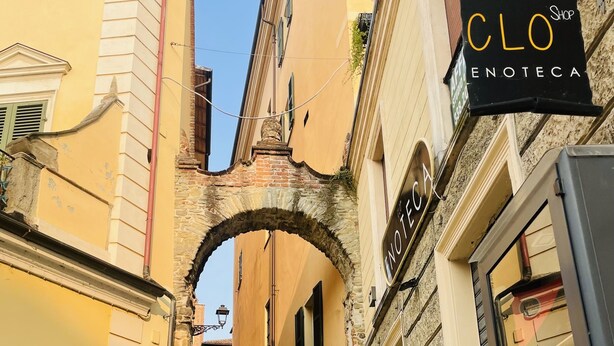 Eine schmale Gasse mit einem steinernen Torbogen, der zu einem Gebäude mit dem Schild 'CLO ENOTEC' führt.