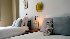 Ein Schlafzimmer mit zwei Betten, einer Wandleuchte, einem gerahmten Pflanzenprint und einem Strohhut.