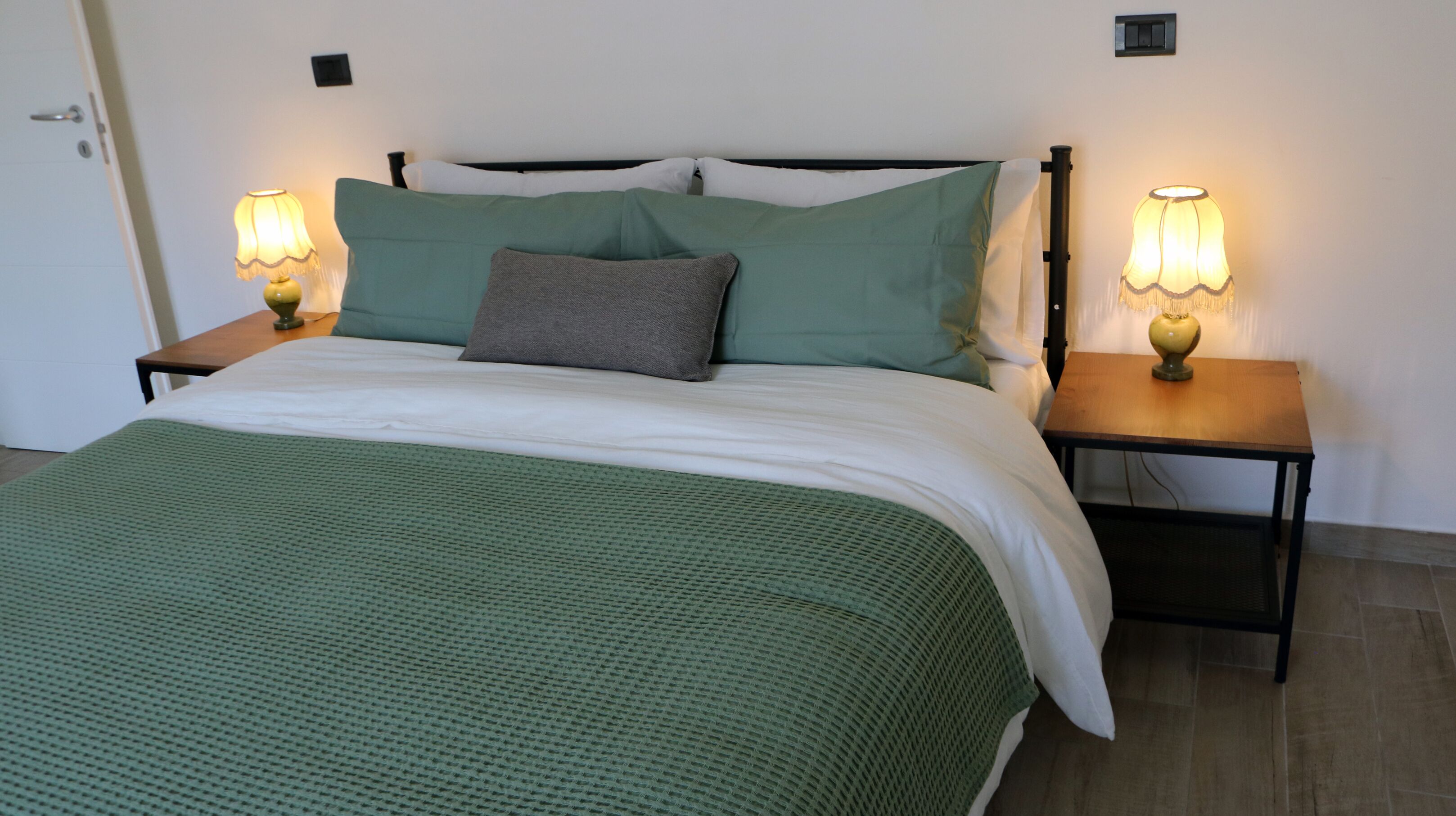 Ein Bett mit einer grünen Decke, zwei Kissen und zwei Nachttischlampen.