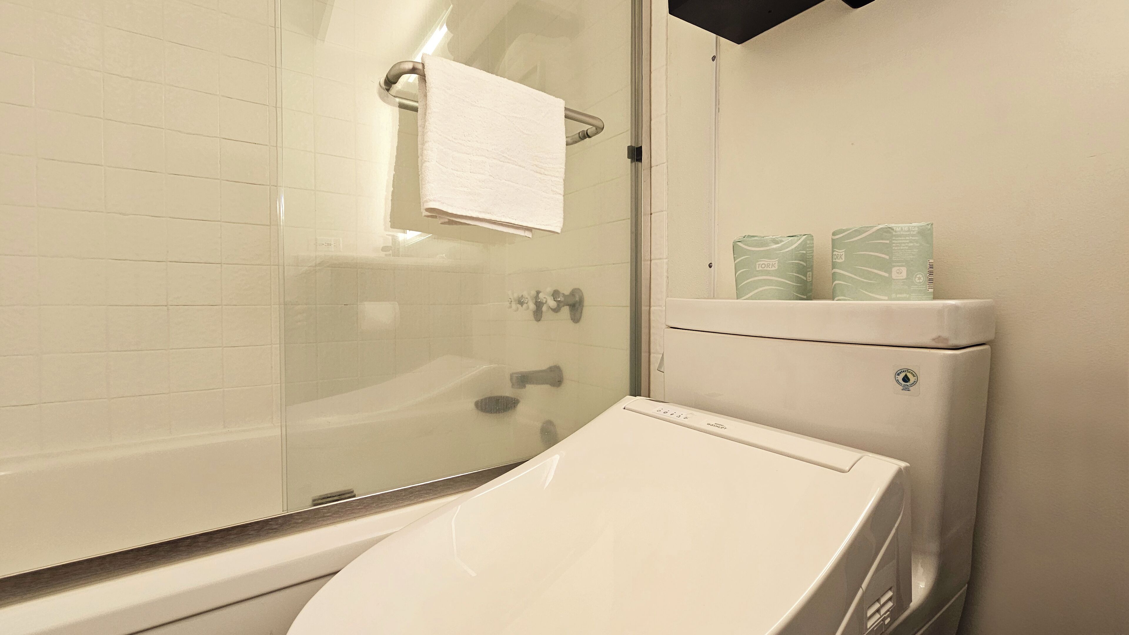 A bathroom with a glass shower enclosure, a white sink, and a toilet with toilet paper.