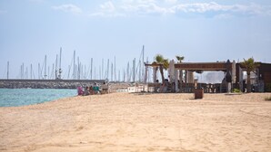 Une plage avec une structure en bois, qui pourrait être un café ou un restaurant, et une rangée de bateaux en arrière-plan.