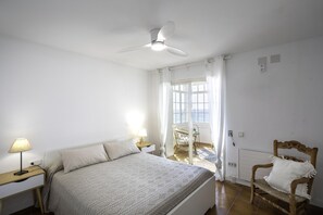 A bedroom with a bed, bedside tables, a chair, a ceiling fan, and a window with curtains. - Victoria - in front of the beach (Sant Vicenç de Montalt)