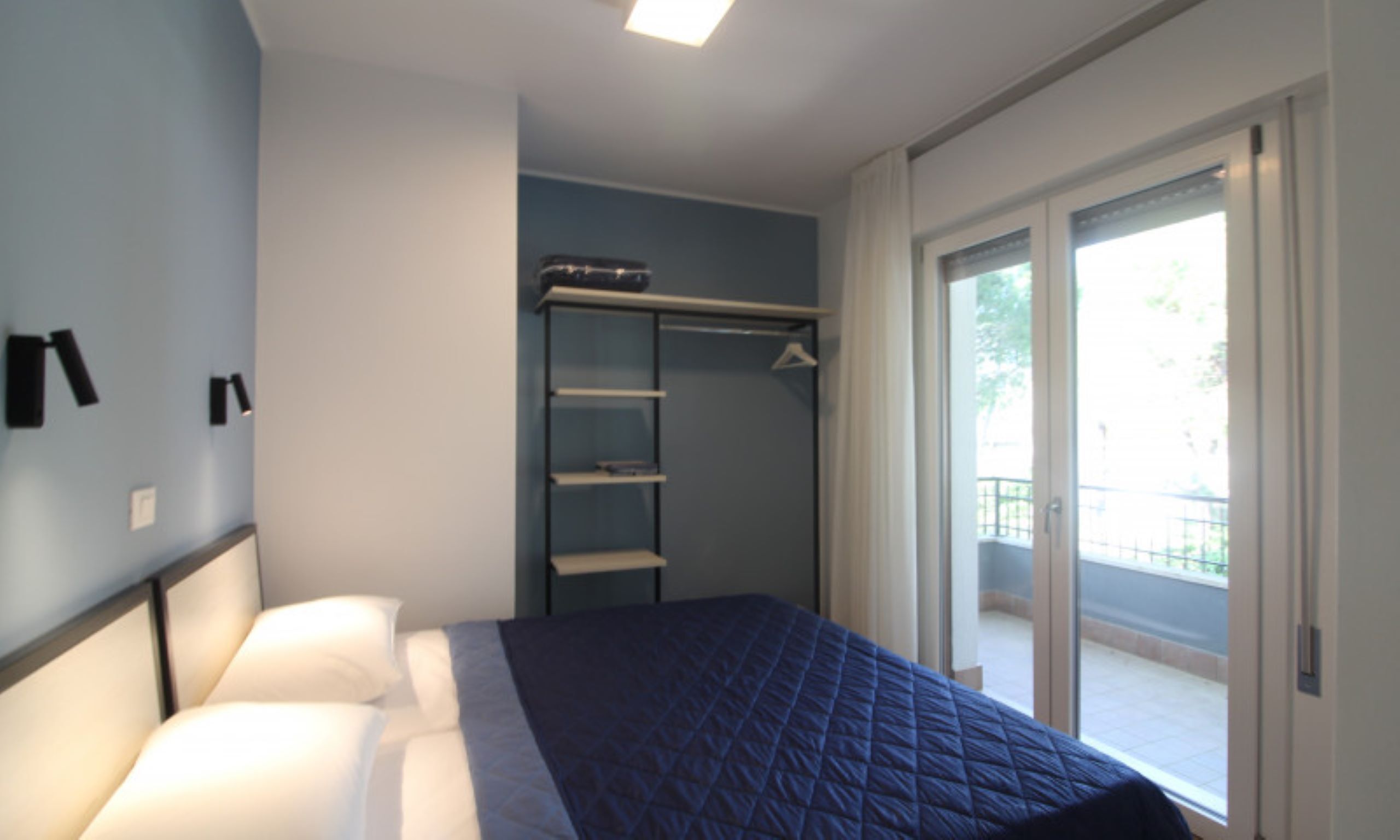 Een slaapkamer met een bed, een garderobe en een glazen schuifdeur naar een buitenruimte.