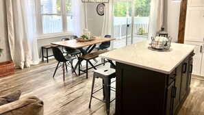 Cucina con isola in marmo, tavolo da pranzo in legno e sedie, con vista su un cortile recintato.