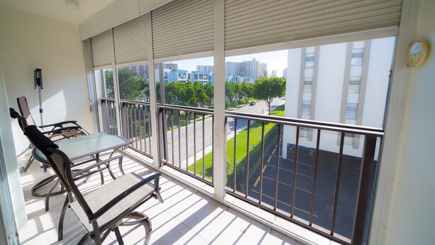 En balkon med et bord og stole, udsigt over bybilledet og en bygning med parkeringsplads.