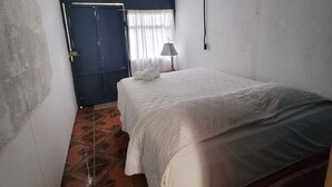 A narrow room with a bed, a door, and a window with curtains. - Hostel A lo Tico (Monte Verde)
