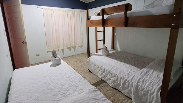 A room with two bunk beds, a wooden door, a window with curtains, and a tiled floor. - Hostel A lo Tico (Monte Verde)