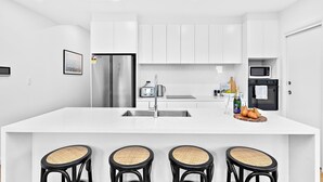 Een moderne keuken met witte kasten, roestvrijstalen apparatuur, een groot eiland met barkrukken, en een kleinere eethoek.