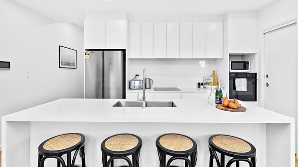 A modern kitchen with white cabinetry, stainless steel appliances, a large island with bar stools, and a small dining area.