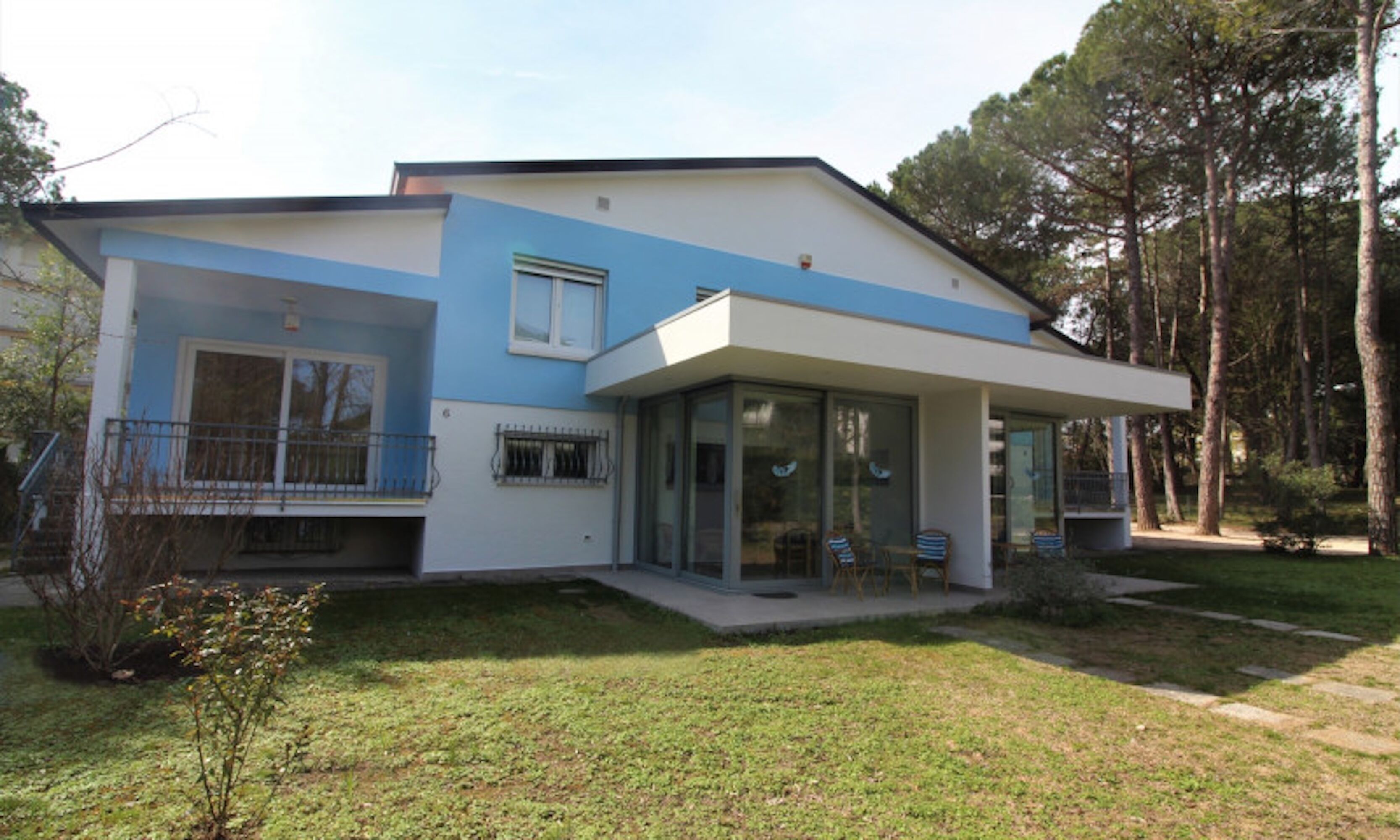 A modern two-story house with a flat roof, large glass windows, and a covered porch with outdoor seating.