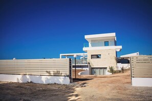 Une maison moderne, avec un ciel dégagé, une allée en terre et une entrée fermée par un portail.