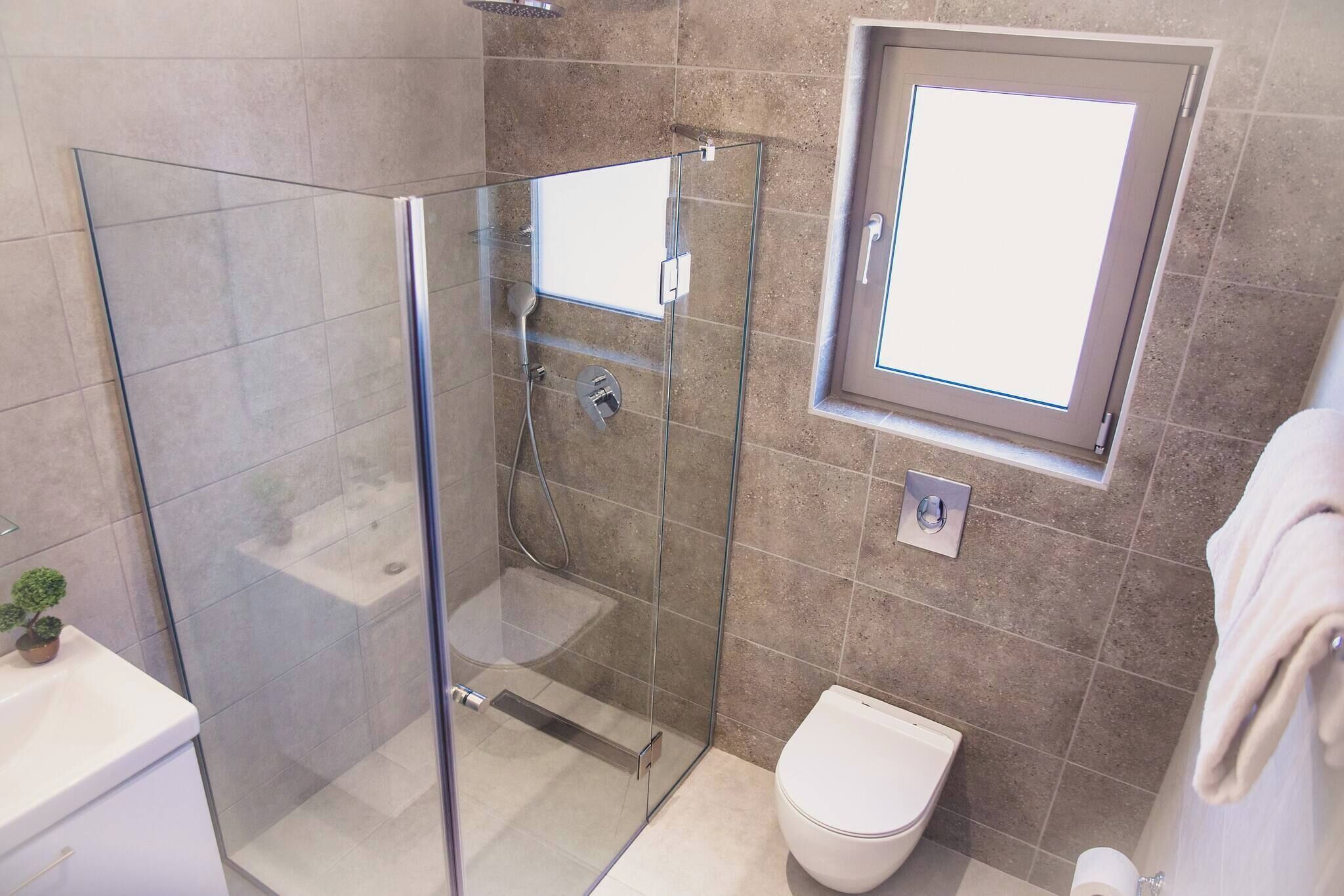 Un baño con ducha de vidrio, inodoro, una ventana pequeña y un perchero para toallas.