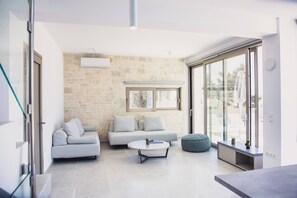 A modern living room with a stone wall, a sofa, a coffee table, and a glass door leading outside. - Starlight Villa Guro - 4bd, 4ba, 4min To Beach (Rethymno)