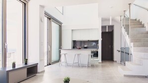 Eine moderne Küche mit weißen Schränken, einer zentralen Kochinsel mit Barhocker und einer Treppe mit Glastrennwand.