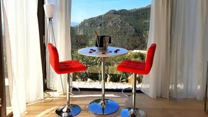 Un balcon avec une table et deux chaises rouges, donnant sur un paysage montagneux.