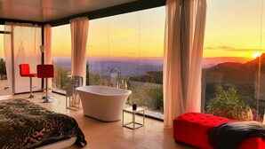 Une chambre à coucher moderne avec une grande fenêtre, une baignoire et un pouf rouge.
