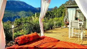 Un lit avec une couvre-lit et des oreillers à motifs rouges, un baldaquin blanc et une vue sur un paysage montagneux.