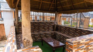A covered outdoor seating area with a bench and a table, surrounded by a patterned wall and a tree trunk. - charming 3-bed apartment in transe ekulu phase 6 (TRANSE EKULU PHASE 6)