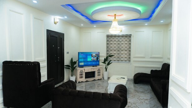 A living room with a television, black sofas, and a marble floor. - charming 3-bed apartment in transe ekulu phase 6 (TRANSE EKULU PHASE 6)
